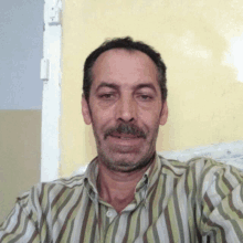 a man with a mustache wearing a striped shirt smiles for the camera