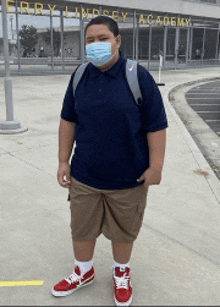 a boy wearing a face mask stands in front of a building that says cherry lindsey academy