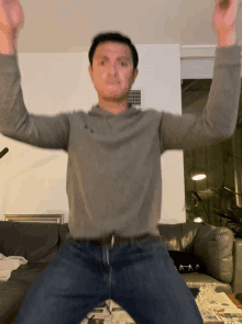 a man in a grey shirt is jumping in the air in front of a couch