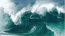 a large wave in the ocean with a blue sky behind it