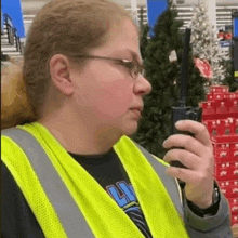 a woman in a yellow vest is talking on a walkie talkie in a store