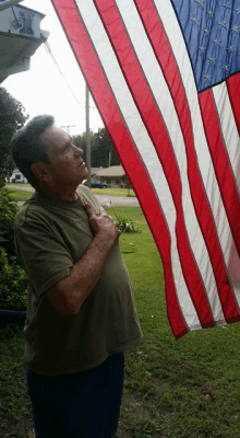 a man holds his hand to his chest while looking up at an american flag