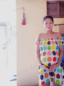 a pregnant woman in a colorful polka dot dress holds her belly