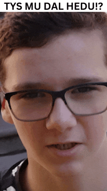 a close up of a young man wearing glasses with the words tys mu dal hedu written above him