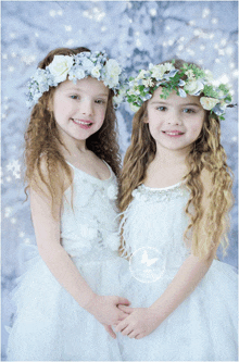 two little girls wearing white dresses and flower crowns are posing for a picture