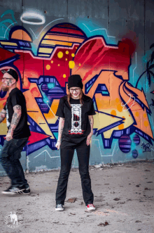 a man and a woman standing in front of a graffiti wall