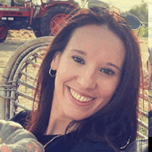 a woman wearing sunglasses smiles while holding a pumpkin in front of a tractor