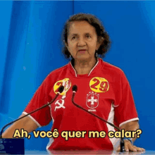 a woman in a red shirt is standing in front of two microphones and talking into them .