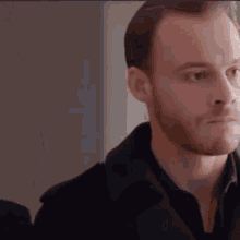 a man with a beard is wearing a black jacket .