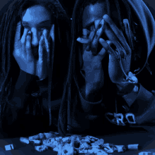 two people with dreadlocks covering their faces with their hands and a pile of cigarette butts