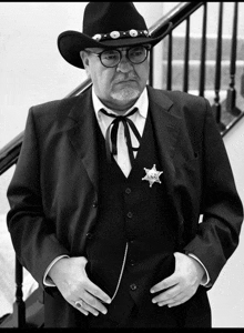 a man in a cowboy hat and vest has a sheriff 's badge