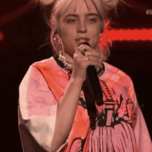 billie eilish is singing into a microphone wearing a pink shirt