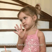 a little girl in a pink dress is sitting on a set of stairs and waving her hand .