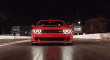 a red dodge demon is driving down a race track at night