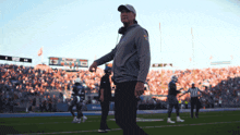 a man walking on a football field with a scoreboard in the background that says ' denver ' on it