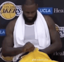 a basketball player with a towel around his neck is sitting in front of a lakers sign .