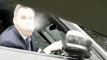 a man in a suit and tie is driving a car with his face visible .