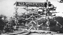 a black and white photo of a group of people standing on top of each other on a tower .