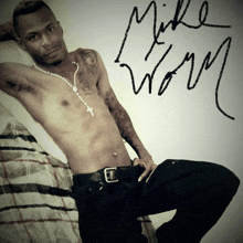 a shirtless man laying on a bed with the name mike wolf written on the wall behind him