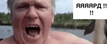 a shirtless man is screaming in front of a body of water with his mouth open .