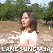 a woman in a pink shirt is standing in a field with the words langsung aja written on the bottom