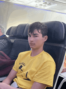 a man wearing a yellow alaska t-shirt sits on an airplane