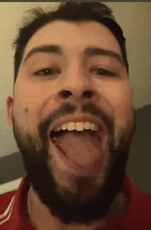 a man with a beard is sticking his tongue out while wearing a red shirt .