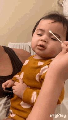 a baby is being brushed with a cotton swab by a woman while wearing a yellow and white polka dot shirt