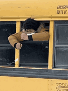 a man wearing a mask looks out of the window of a yellow school bus