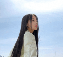 a woman with long black hair is wearing a white shirt and earrings and looking up at the sky .