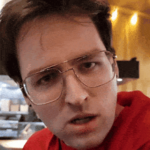 a man wearing glasses and a red shirt is making a face