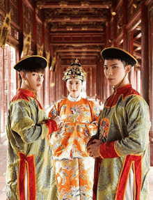 a woman in an orange dress is standing between two men in traditional costume