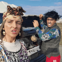 a man and a woman standing in front of a car with the hood open