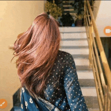 a woman with long brown hair is standing on a set of stairs with her hair blowing in the wind .