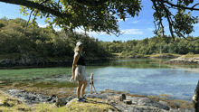 a woman stands on a rock near a lake