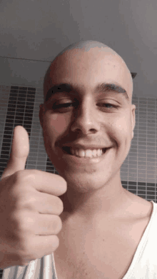 a smiling man with a shaved head giving a thumbs up