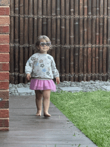 a little girl wearing heart shaped sunglasses is walking on a wooden walkway