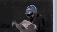 a man in a suit and tie is reading a newspaper while wearing a helmet .