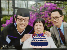 a picture of a man in a graduation cap and gown with two men and a cake with candles on it