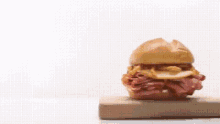 a sandwich is sitting on a wooden cutting board on a white surface .