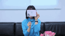 a woman in a blue sweater is covering her face with a valentine 's day card