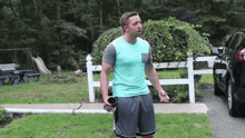 a man in a blue shirt and shorts is standing in front of a white fence holding a cup .