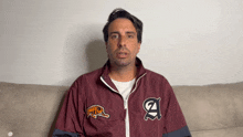 a man wearing a maroon jacket with the letter a on it sits on a couch