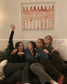 a group of young women are sitting on a couch in front of a framed picture of a group of people