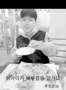 a boy sitting at a table with a plate of food and a box of pizza with korean writing on the bottom