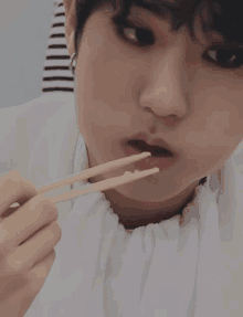 a young boy is eating food with chopsticks and making a funny face .