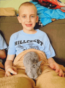 a boy wearing a blue shirt that says hillcrest is holding a small rabbit