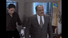 a man in a suit and tie is walking in front of a sony television