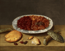 a plate of dried fruit sits on a wooden table next to some bread