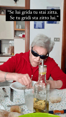 an older woman wearing sunglasses sits at a table with a bottle of oil